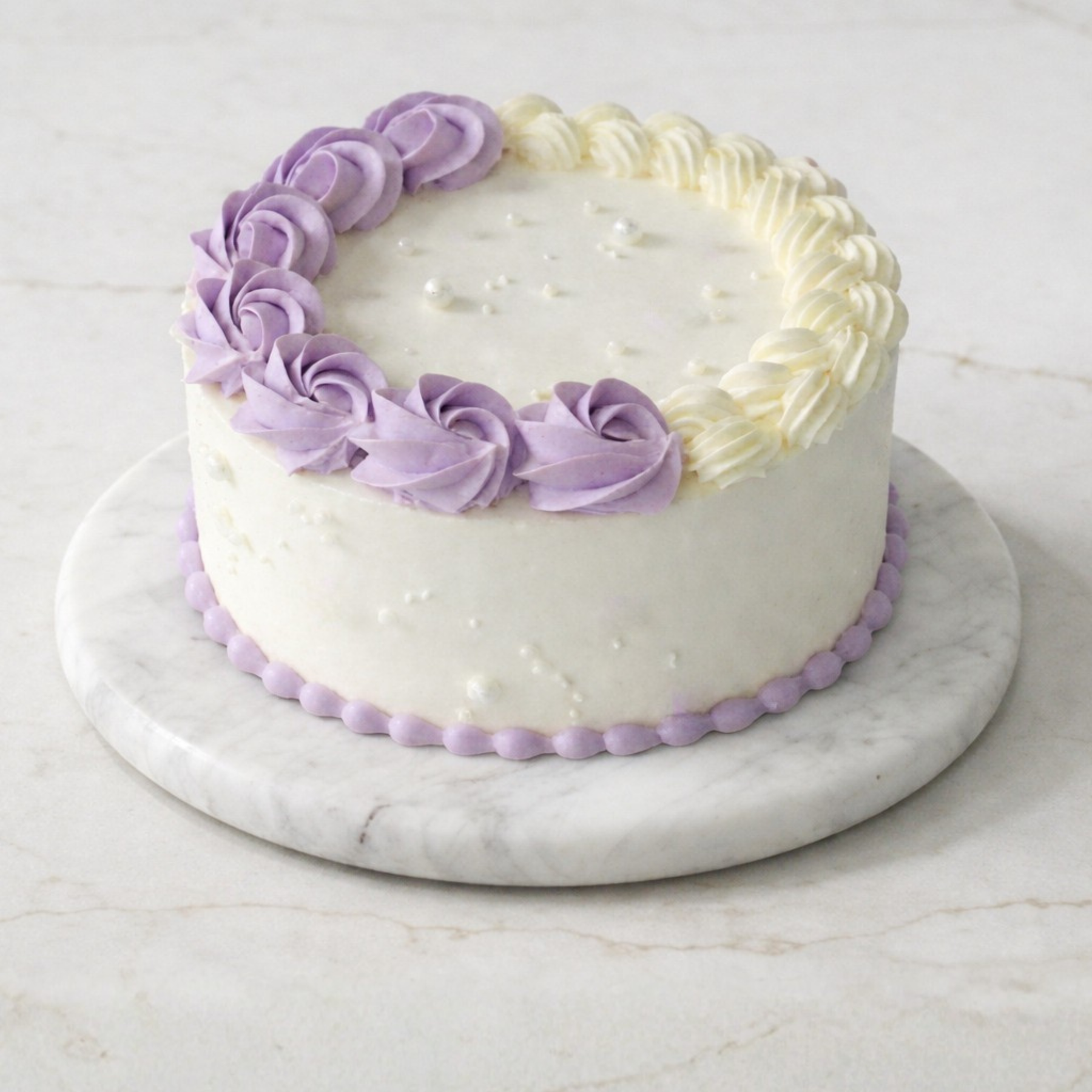 White cake with purple decorative icing on a marble stand