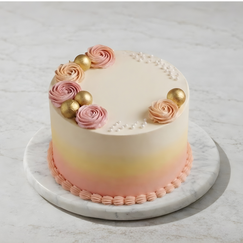 Elegant ombré cake with pink-to-peach gradient, gold spheres, and pink rosettes on white marble base.