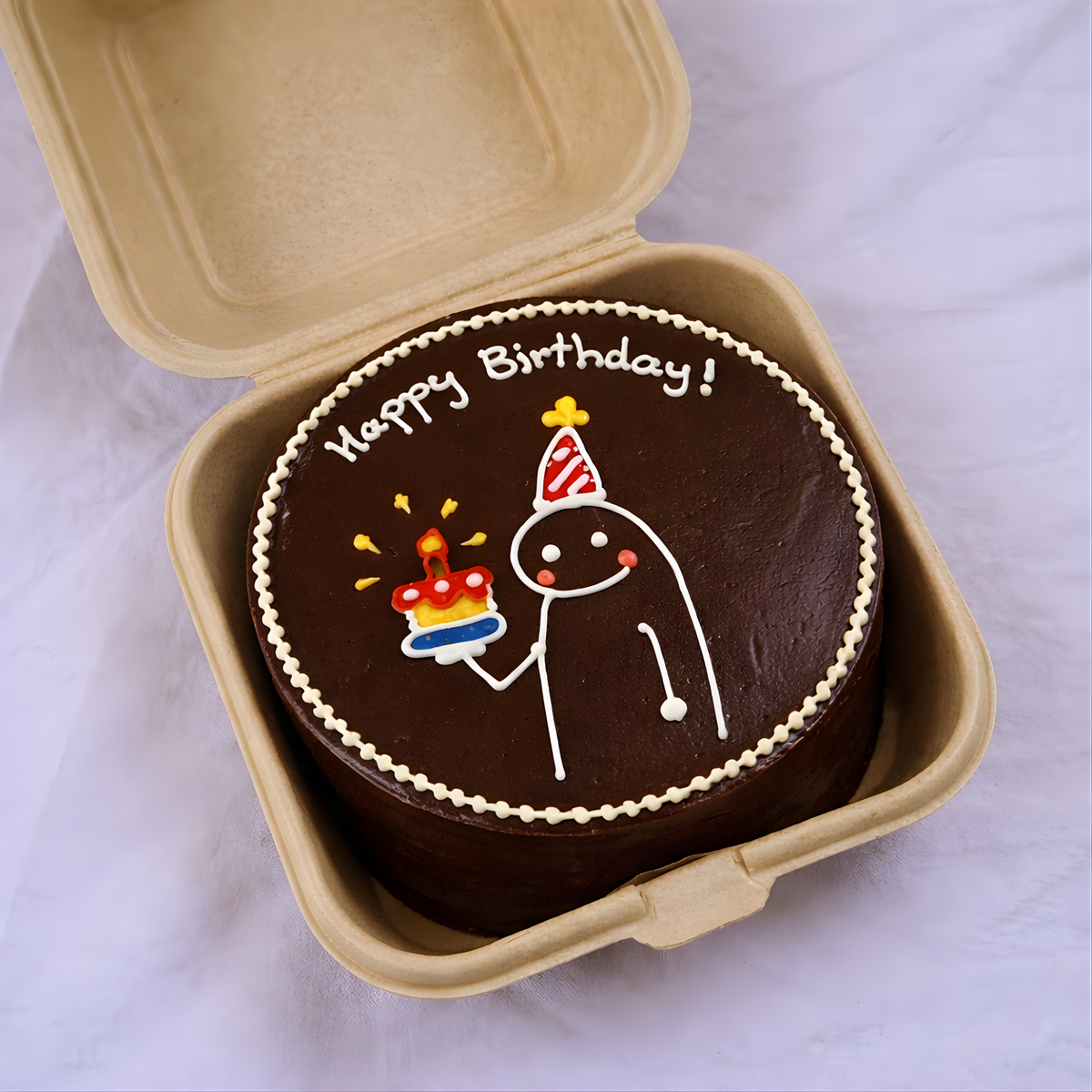 Chocolate birthday cake with cartoon character and 'Happy Birthday!' text in a cardboard box.