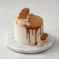 Biscoff Luxe Cake with caramel drip, piped rosettes, and Biscoff pieces on marble stand.