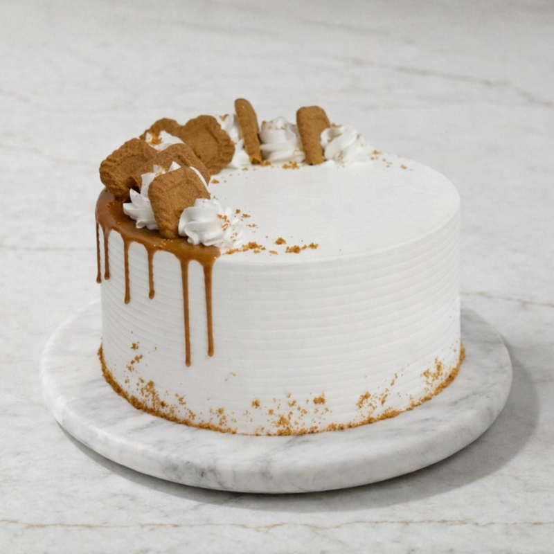 White cake with caramel drip, Biscoff crumbs, and white piping, topped with Biscoff pieces on a marble platter.