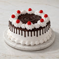 Black Forest drip cake with whipped cream, chocolate ganache, and cherries on top of a marble cake stand.