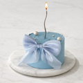 Blue cake with a white bow and lit candle on a marble stand against a light background