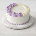 White cake with purple decorative icing on a marble stand
