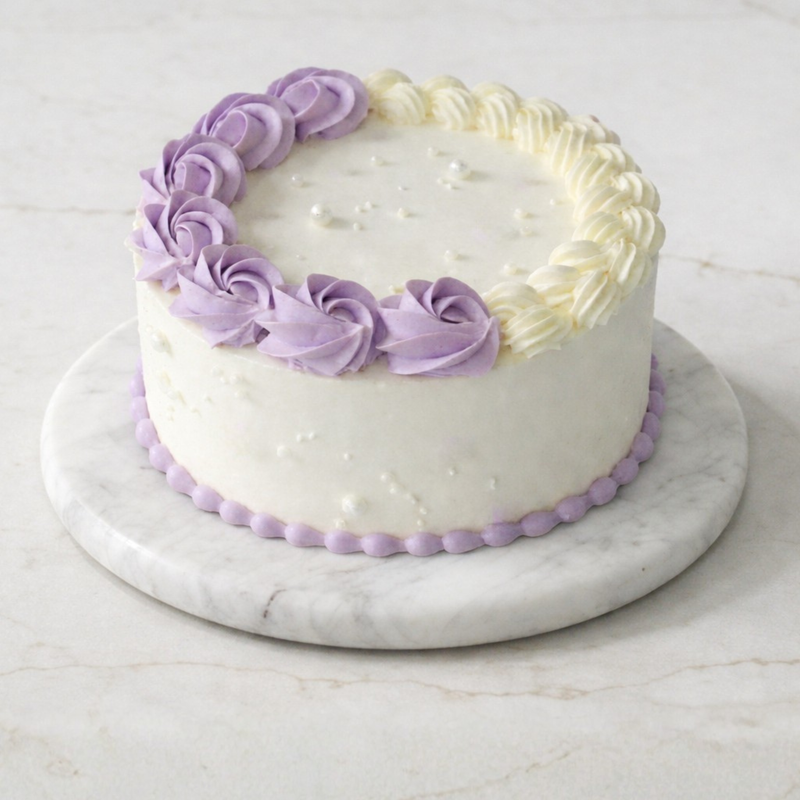 White cake with purple decorative icing on a marble stand