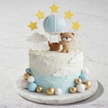 Decorative cake with teddy bear, hot air balloon, and stars on a marble surface