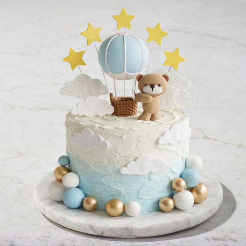 Decorative cake with teddy bear, hot air balloon, and stars on a marble surface