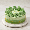 Green ombré cake with piped rosettes and gold pearl accents on a marble stand.