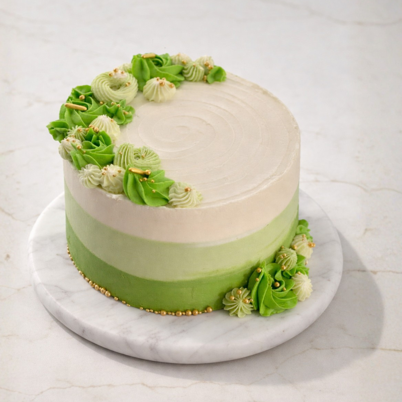 Pastel cake with pale-to-green gradient, decorated with green rosettes and gold pearl accents on a marble base.