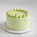 Pistachio cake with green textured layers, topped with piped rosettes and crushed pistachios on marble platter.