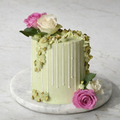 Pale green cake with pink and white roses, vertical stripes, and ornate piping on a marble platter.