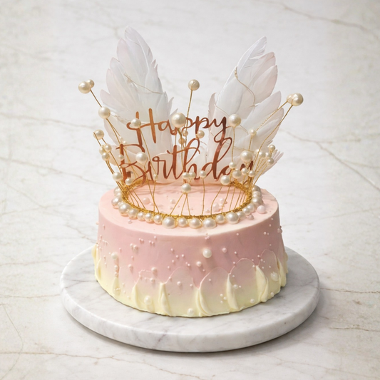 Pink birthday cake with feather decorations and 'Happy Birthday' topper on a marble stand.