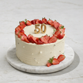 White cake with strawberries and a gold number 50 on a marble surface